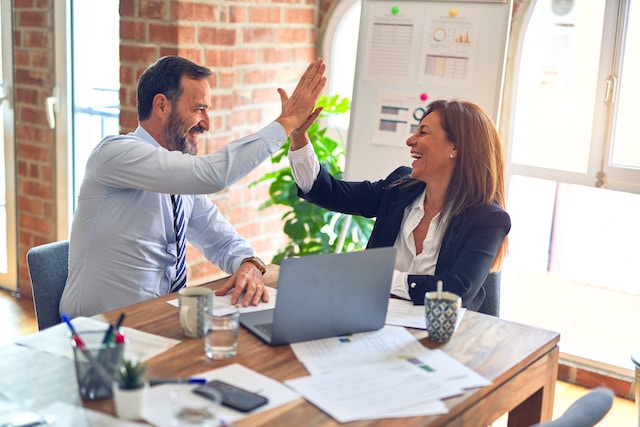 Two corporate employees sitting while smiling and high-fiving