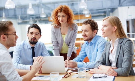 Group of business partners looking at young man presenting computer project at meeting