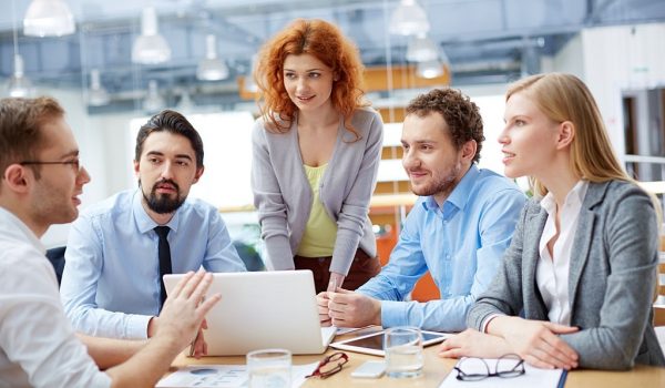 Group of business partners looking at young man presenting computer project at meeting