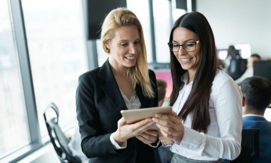 Portrait of two attractive businesswomen using tablet in modern office