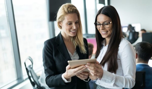 Portrait of two attractive businesswomen using tablet in modern office